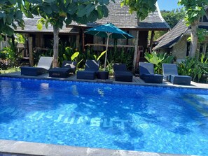 A swimming pool with lounge chairs and an umbrella, surrounded by tropical plants and a wooden building. - Green Villas Lembongan by ABM (Lembongan Island)