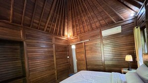 Habitación con paneles de madera, una cama, una mesita de noche y un equipo de aire acondicionado montado en la pared.