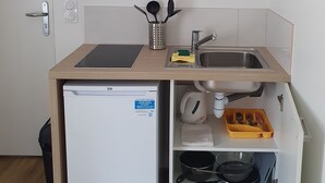 A compact kitchenette with a built-in dishwasher, a coffee maker, a sink, and a small refrigerator.