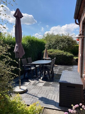 An outdoor patio with a table and chairs, a covered umbrella, and a small barbecue grill.