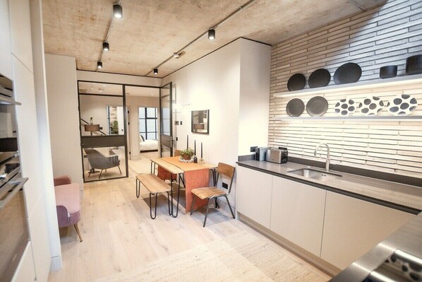 A modern kitchen with a wooden backsplash, a dining area with a table and chairs, and a visible kitchen counter with a sink.