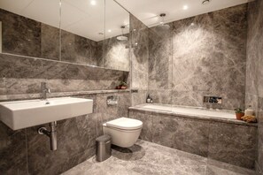 A modern bathroom with a marble wall, a sink, a toilet, and a shower.