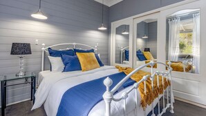 Un dormitorio con cama, mesita de noche, lámpara y un espejo grande que refleja la habitación.