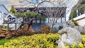 Una estatua de piedra en un jardín con flores amarillas, un muro de piedra y un edificio con una escalera al fondo.