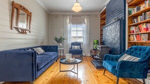 Una sala de estar acogedora con un sofá azul, un sillón azul, una mesita redonda y una estantería llena de libros.
