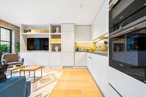 A modern kitchen with white cabinetry, a built-in oven, and a dining area with a sofa and coffee table.