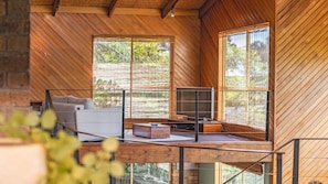 Relax in this spacious living area with a panoramic view of the surrounding greenery, featuring a comfortable seating area and a flat-screen TV.