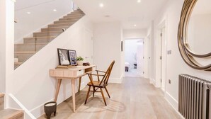 Un interior modern amb una escala, un escriptori amb una cadira i un mirall gran.