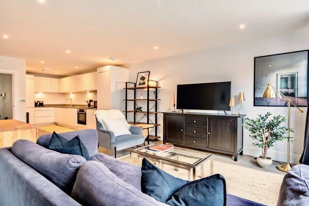Ein modernes Wohnzimmer mit einem grauen Sofa, einem Couchtisch, einem Fernseher und einem Bücherregal.