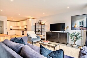 Una sala de estar moderna con un sofá gris, una mesa de centro, un televisor y una estantería.