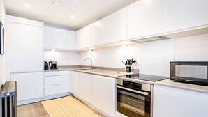 Eine moderne Küche mit weißen Schränken, einem eingebauten Backofen, einer Mikrowelle und einer Kaffeemaschine.