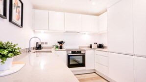 A modern kitchen with white cabinets, a built-in oven, a coffee maker, and a potted plant.