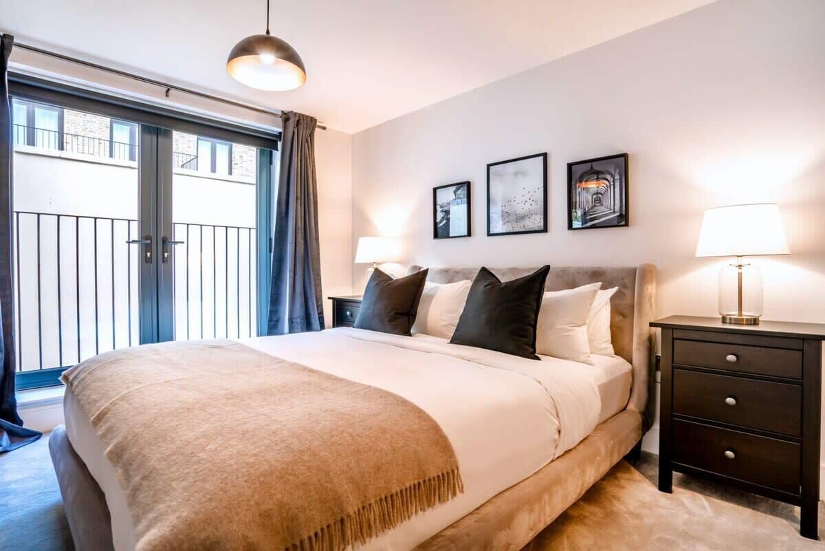 A bedroom with a large bed, a nightstand, a lamp, and a view of the outside.