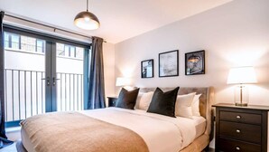 A bedroom with a large bed, a nightstand, a lamp, and a view of the outside.