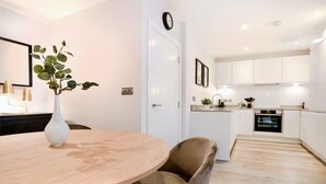 A modern kitchen with white cabinets, a built-in oven, and a dining area with a round table and a single chair.
