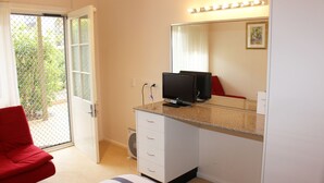 Una camera d'albergo con una porta-finestra scorrevole che dà su un balcone, una scrivania con un computer, uno specchio e una sedia rossa.