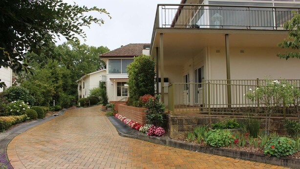 Una strada residenziale con case, un vialetto pavimentato e giardini curati.