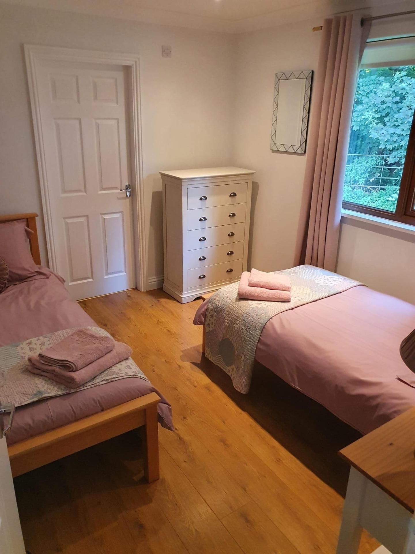 Een slaapkamer met twee bedden, een kaptafel en een raam met uitzicht op begroeiing.