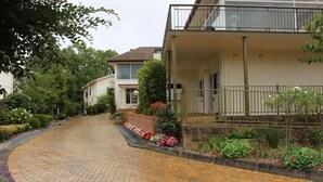 Een woonstraat met huizen, een geplaveid oprit en diverse planten en bloemen.