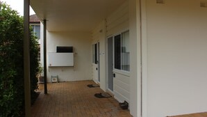 Een overdekt buitengebied met een stenen vloer, een witte muur en een deur met een raam.