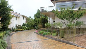 Een geplaveid pad leidt naar een woonhuis met een omheinde tuin en een balkon.