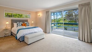 Ein Schlafzimmer mit einem großen Bett, einem Nachttisch, einer Bank, einem Fenster mit Blick auf Grünflächen und einem Balkon mit Geländer.