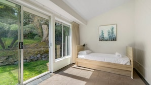 Ein Schlafzimmer mit einem hölzernen Bett, einem Bild an der Wand und Blick auf einen Garten durch große Schiebeglastüren.