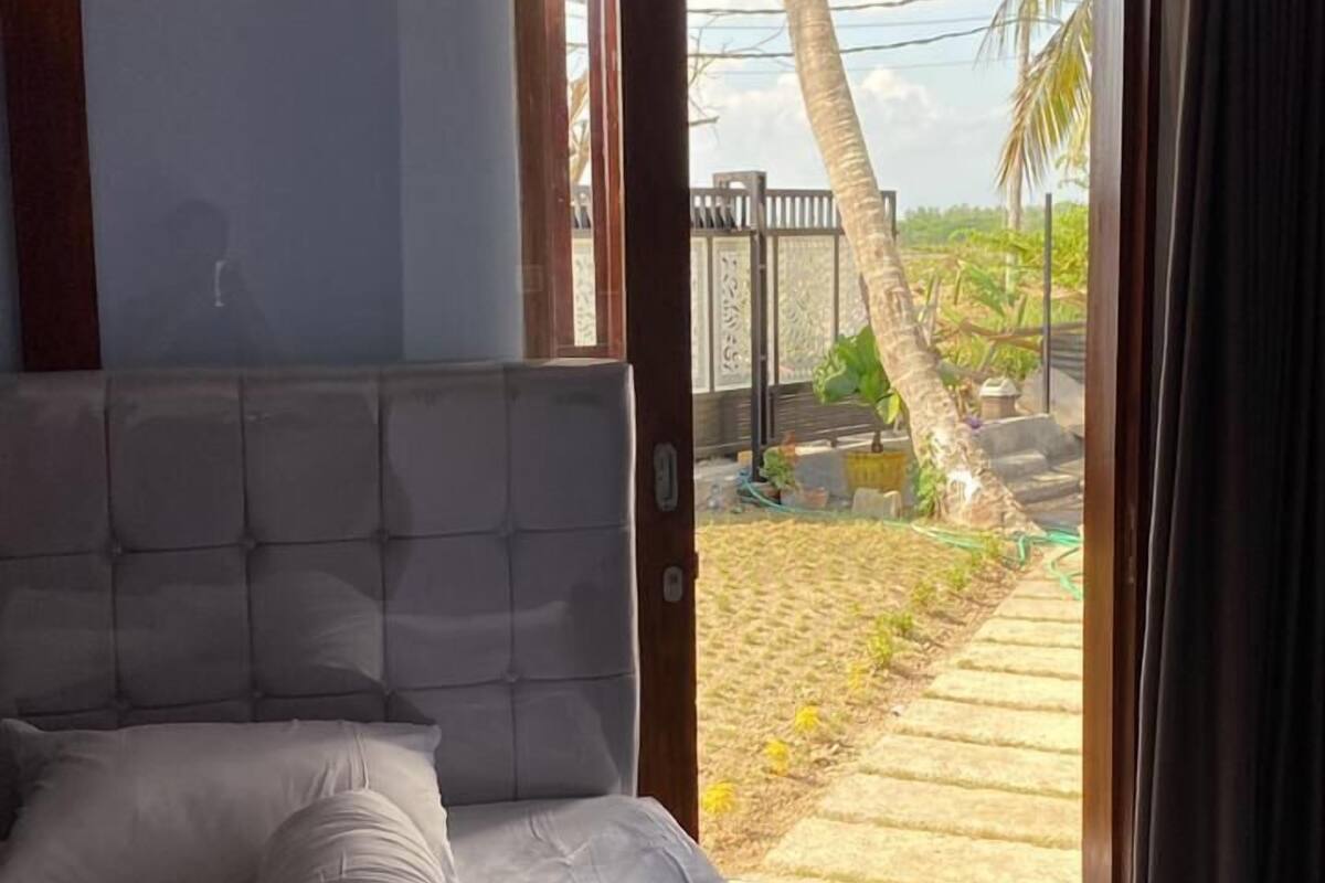 A bedroom with a bed, a view of a garden through an open door, and a view of the sky.
