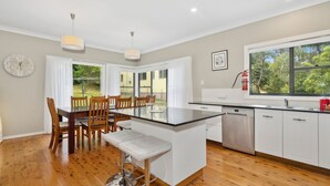 Une cuisine moderne avec un îlot central, une table à manger en bois et des chaises. Une fenêtre offre une vue sur la verdure à l’extérieur.