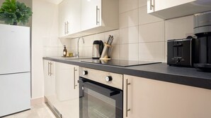 A modern kitchen with white cabinets, a black countertop, a built-in oven, and a coffee maker.