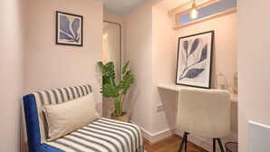 A bedroom with a bed, a chair, a potted plant, and framed artwork on the wall.