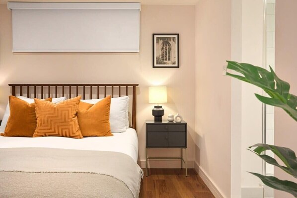 A neatly arranged bedroom with a bed, bedside table, lamp, and a framed picture on the wall.