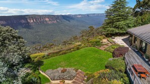 Een huis met uitzicht op een canyon, een verzorgd gazon en een houten terras met buitenmeubilair.