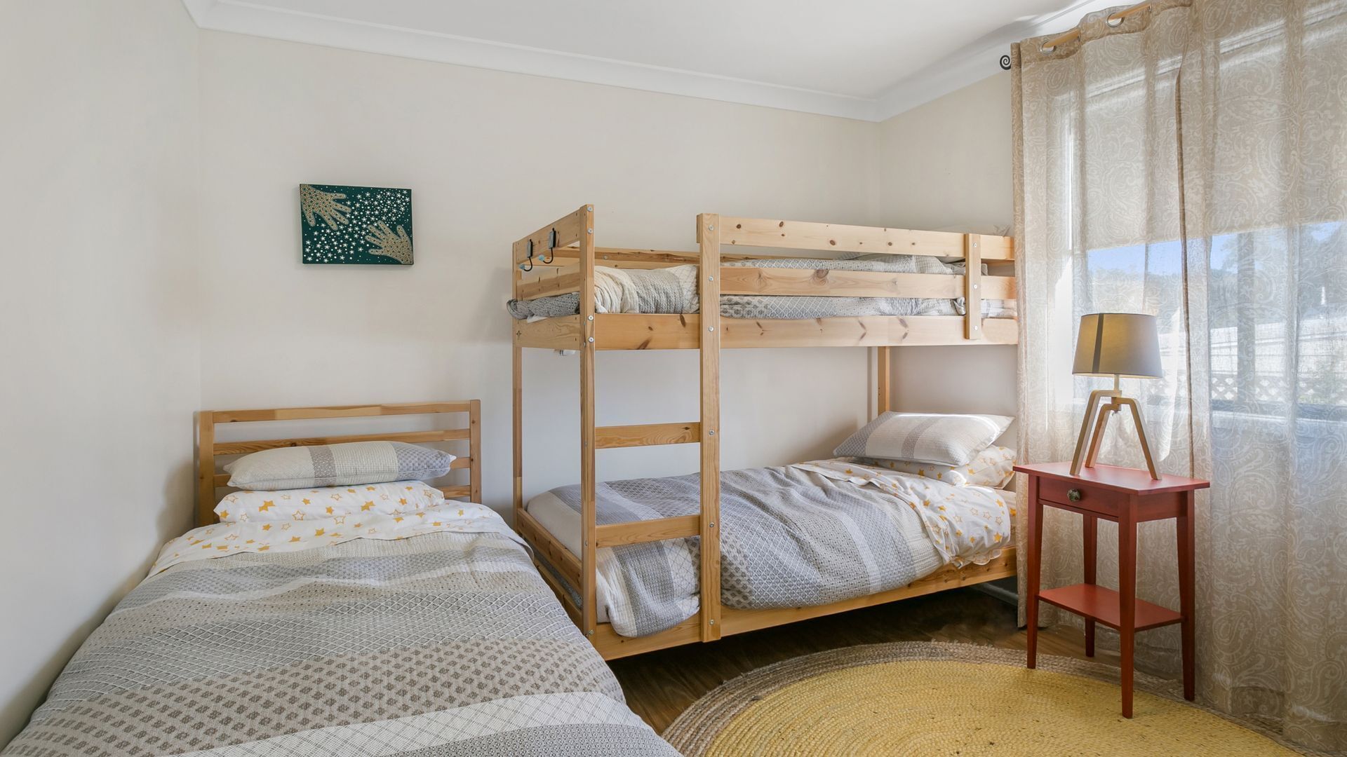 A room with two bunk beds, a small table with a lamp, and a decorative wall piece.