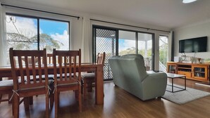 A spacious living area with a dining table, chairs, a sofa, a TV, and large windows offering a view of the outdoors. - Emerald View @ Katoomba (Katoomba)