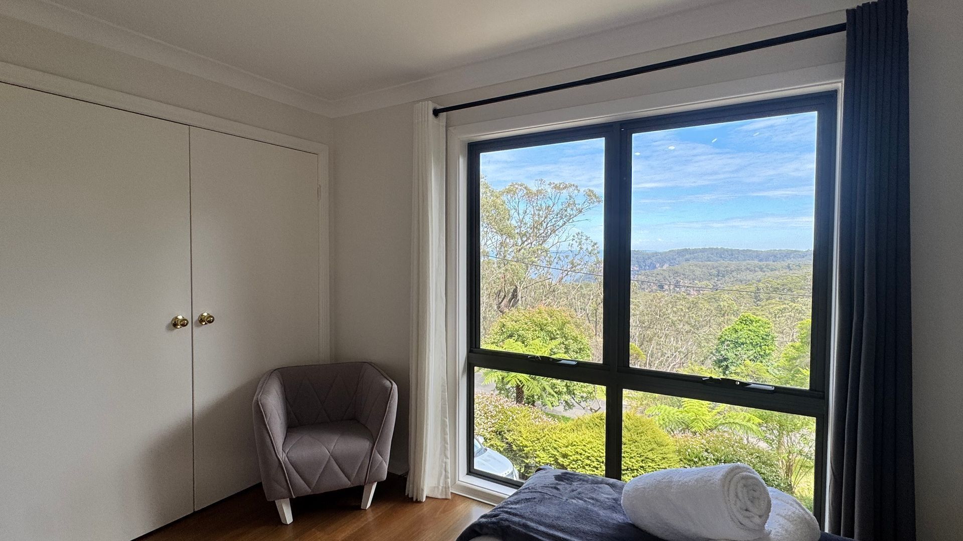 A bedroom with a large window, a chair, and a bed.