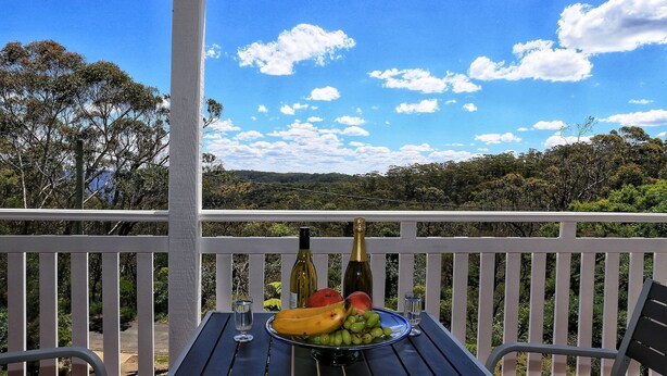 A balcony with a table set for a meal, including a bottle, wine glass, and fruit. - Emerald View @ Katoomba (Katoomba)