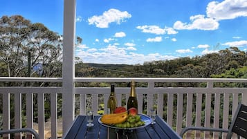 A balcony with a table set for a meal, including a bottle, wine glass, and fruit.