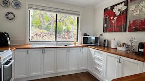 A kitchen with white cabinets, a wooden countertop, a microwave, a kettle, and a window with a view of greenery. - Emerald View @ Katoomba (Katoomba)