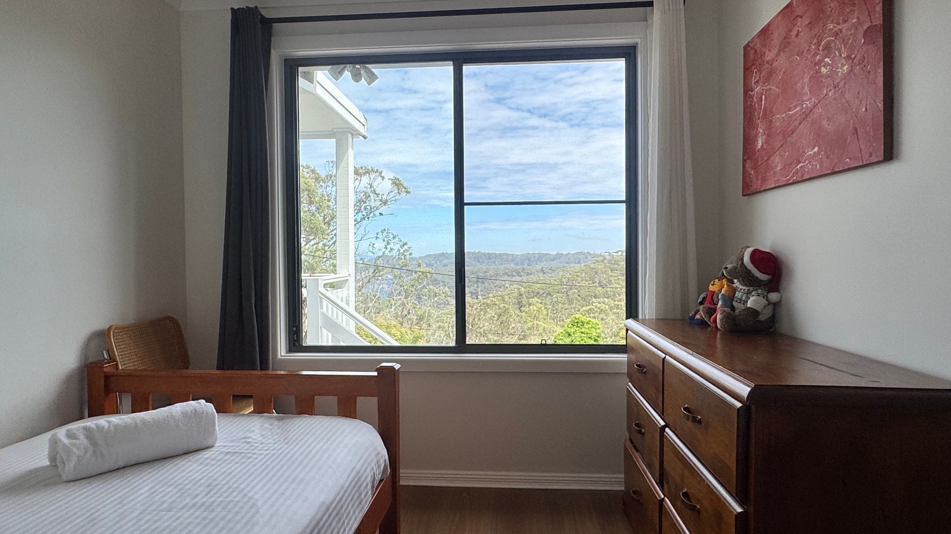 A bedroom with a large window, a bed, a dresser, and a view of the outdoors.