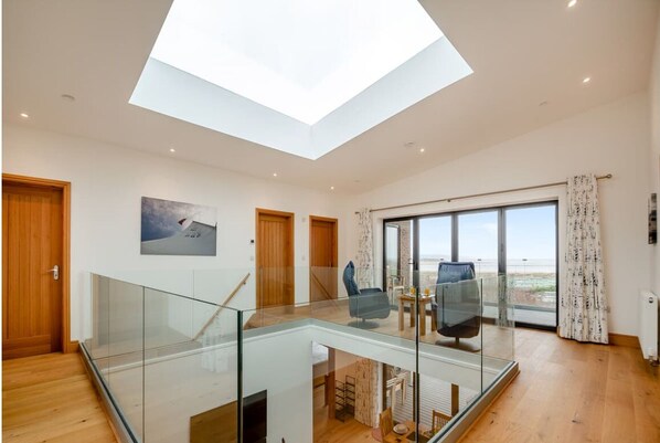 A spacious living area with a glass staircase, a large skylight, and a view of the beach.