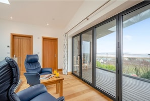 A modern room with a wooden floor, two wooden doors, a glass sliding door leading to a balcony, and a view of the sea.