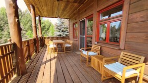 A wooden deck with a table and chairs, a bench, and a window with red trim.