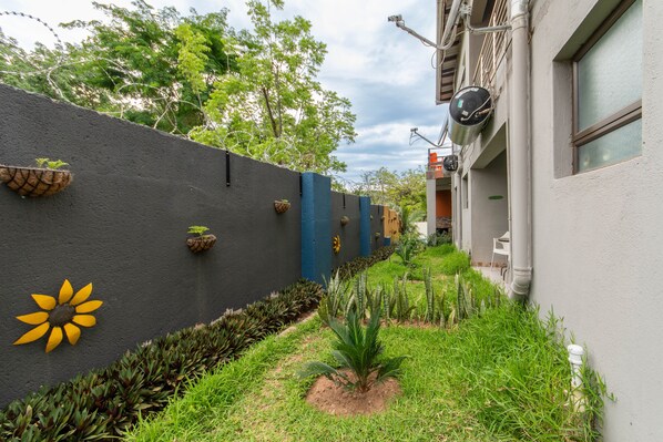 Un callejón estrecho con una pared negra decorada con macetas y un adorno floral amarillo.