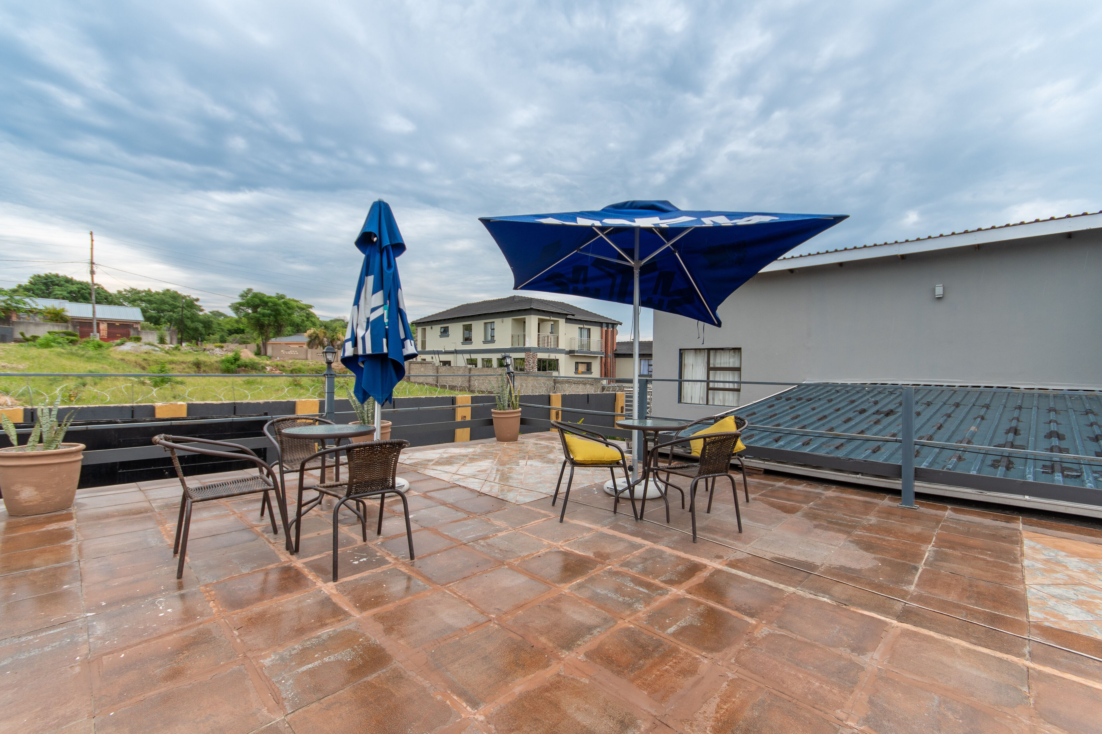 Een terras op het dak, met een tafel, stoelen, een blauwe parasol en gebouwen op de achtergrond.