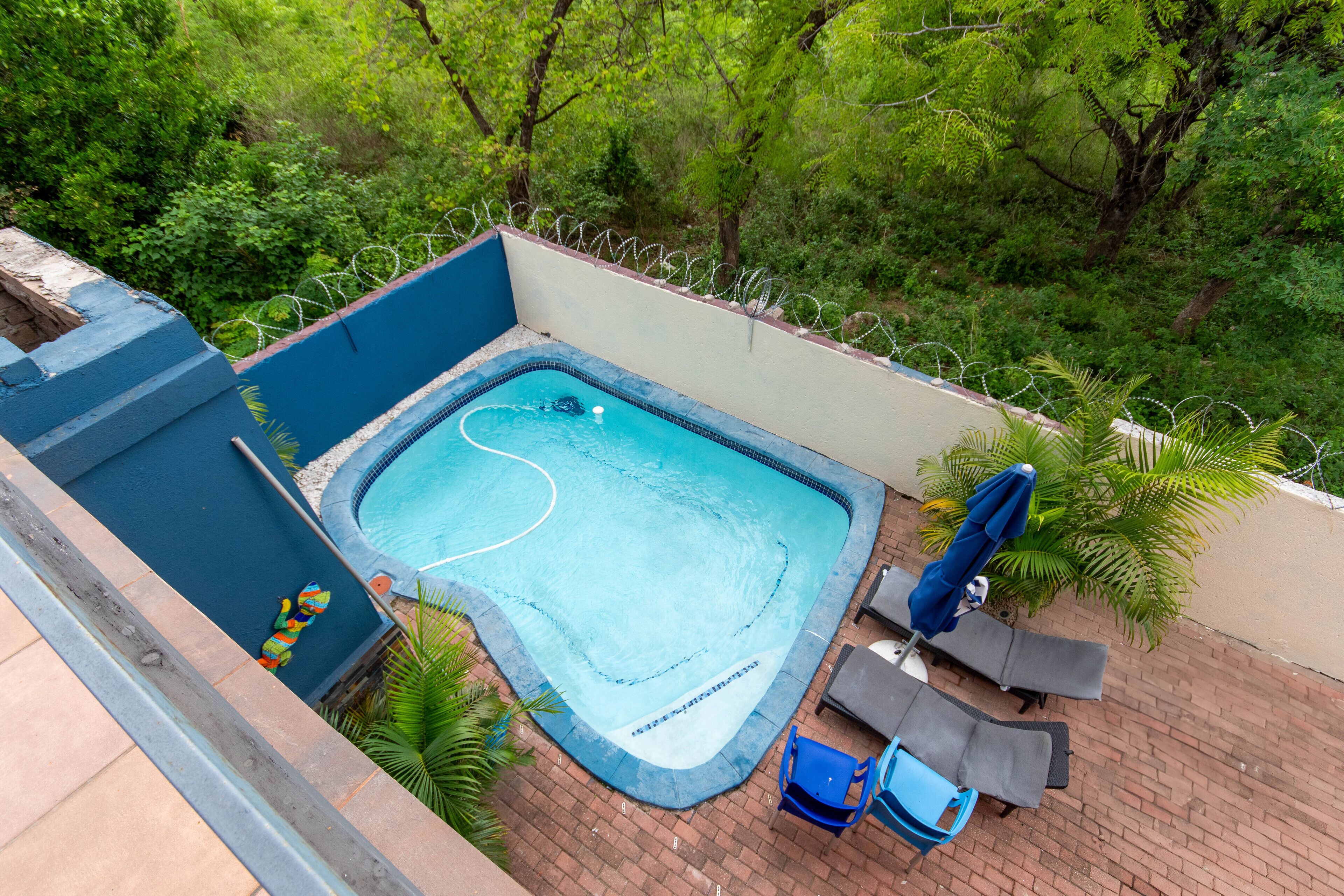 A rectangular swimming pool with a blue interior, surrounded by a brick patio and a low white wall with barbed wire.