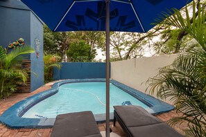 A small swimming pool with a blue border, surrounded by a brick patio and a blue umbrella. - Woodpeckers Guest House (Mbombela)
