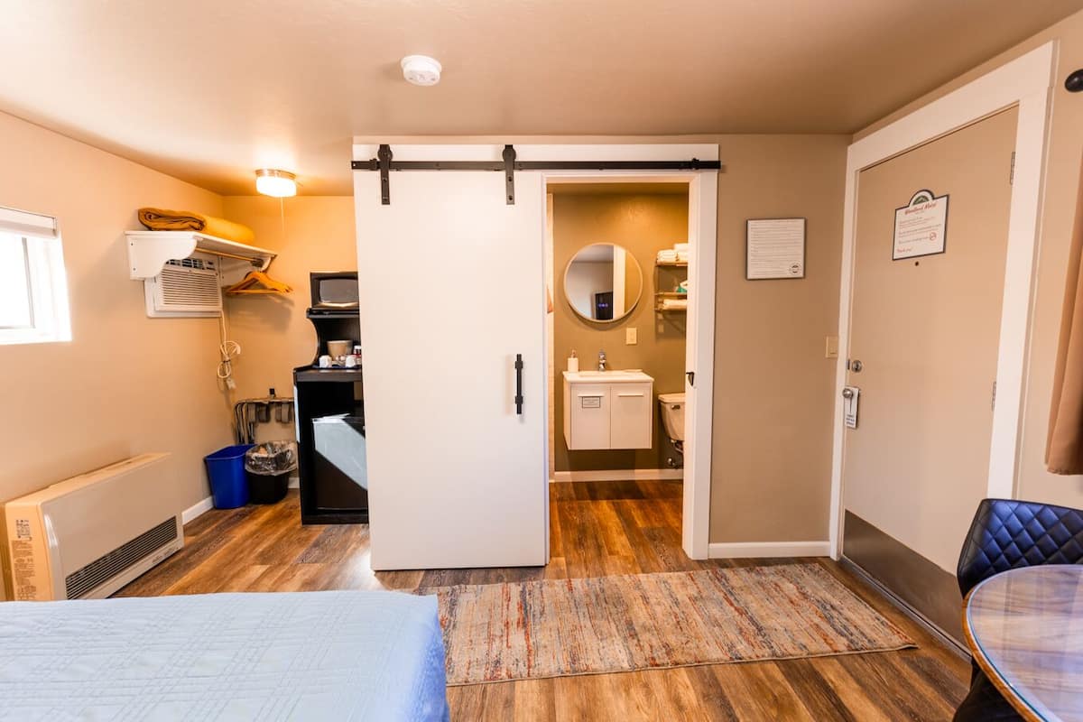 A hotel room with a bed, a desk with a computer, a bathroom with a sink and toilet, and a sliding door leading to another room.