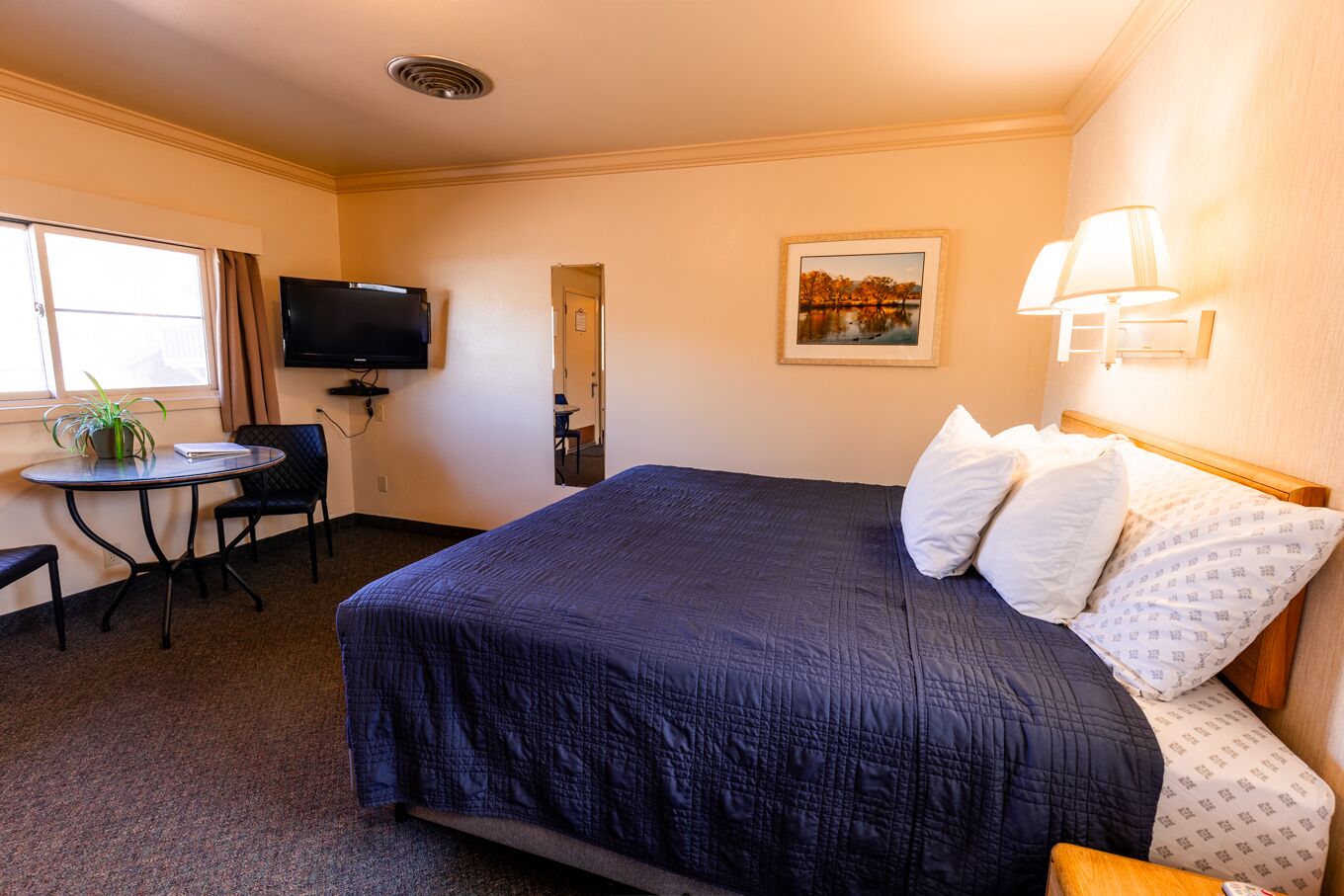 Una habitación de hotel con una cama grande, un escritorio con silla, un televisor y una ventana con cortinas.