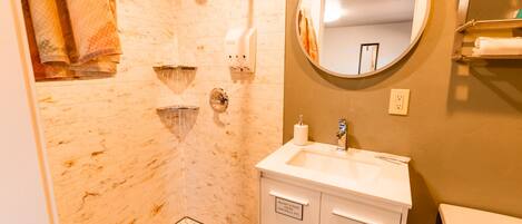A bathroom with a shower, a sink, a toilet, and a mirror.
